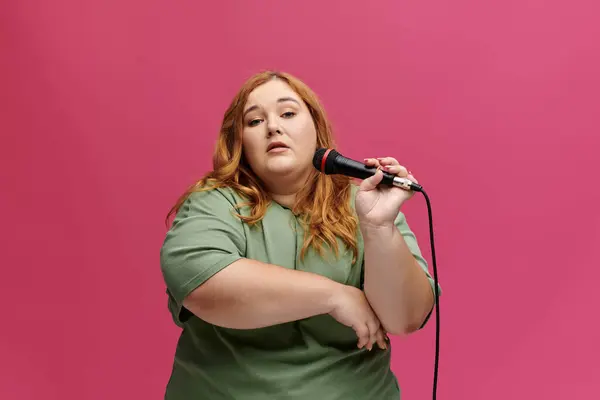 Femme pose avec confiance en t-shirt vert, tenant un microphone et regardant la caméra — Photo de stock