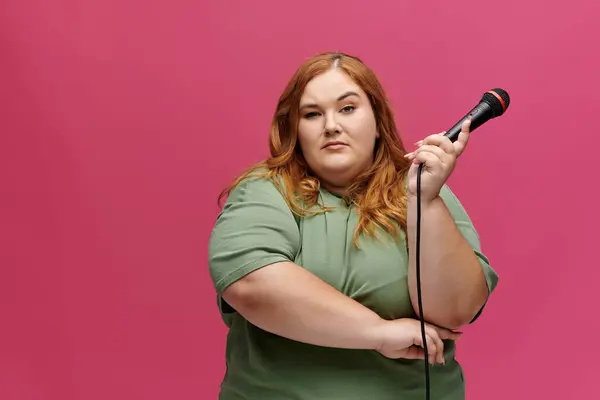 Eine Frau im grünen Hemd hält selbstbewusst ein Mikrofon vor rosa Hintergrund. — Stockfoto