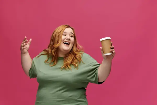 A woman laughs and holds a coffee cup in front of a pink background. — Stock Photo