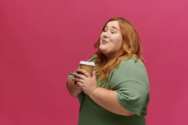 A woman with long red hair smiles as she holds a coffee cup to her chest. — Stock Photo