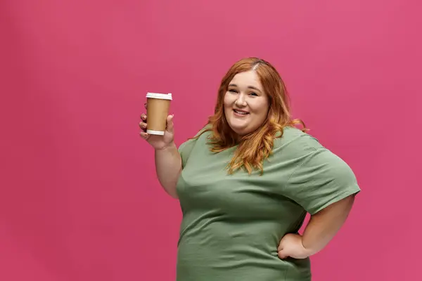 A woman in a green t-shirt holds a cup of coffee and smiles brightly. — Stock Photo