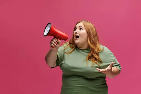 Eine Frau mit langen roten Haaren und grünem Hemd hält ein Megafon in der Hand und schreit. — Stockfoto