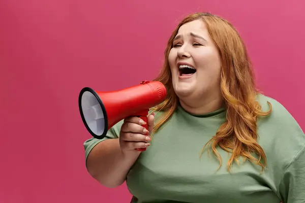 Eine Frau mit langen, roten Haaren lächelt und ruft durch ein Megafon. — Stockfoto