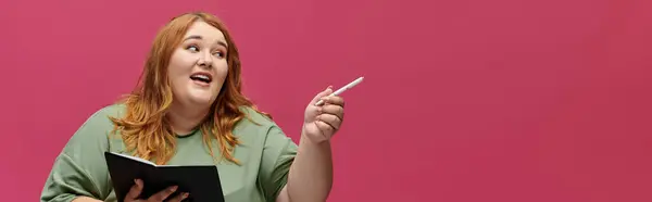 A woman with long red hair gestures enthusiastically while holding a notebook. — Stock Photo