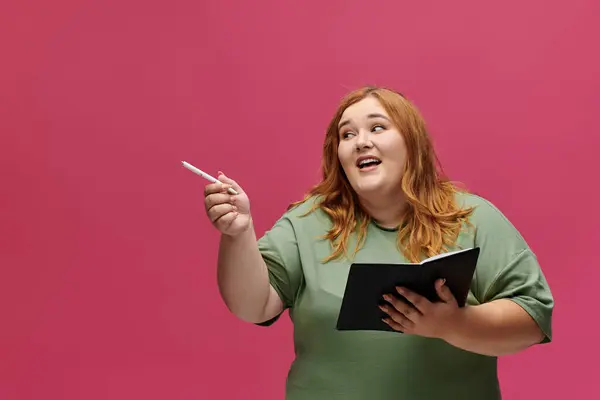A woman with long red hair presents while holding a notebook and pen. — Stock Photo