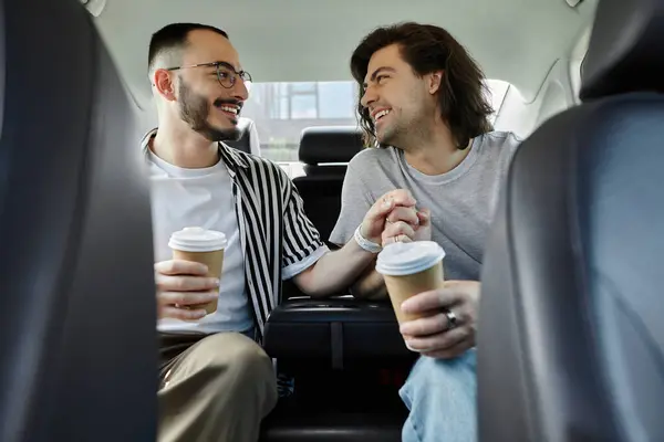 A gay couple enjoys a coffee date in the backseat of a car, holding hands and smiling at each other. — Stock Photo