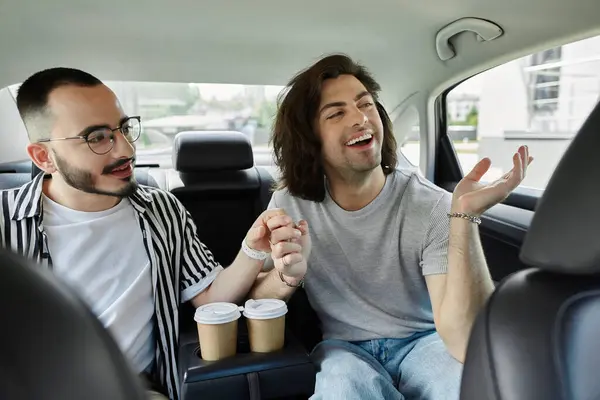A gay couple in the back seat of a car smiles and holds hands while drinking coffee. — Stock Photo