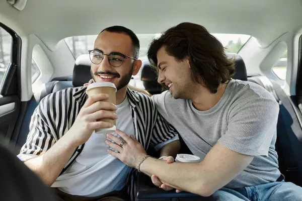 A gay couple laughs and enjoys a coffee date in the backseat of a car. — Stock Photo