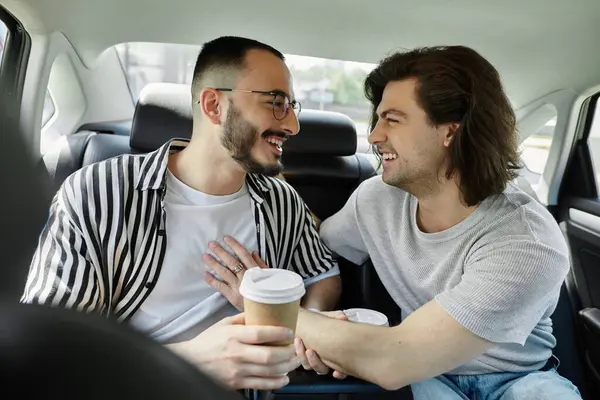 A gay couple laughs together in the backseat of a car, enjoying coffee. — Stock Photo