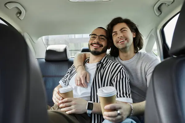 A happy gay couple enjoys a coffee date, laughing together in the backseat of a car. — Stock Photo