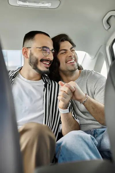 A gay couple hold hands and laugh together in the backseat of a car. — Stock Photo