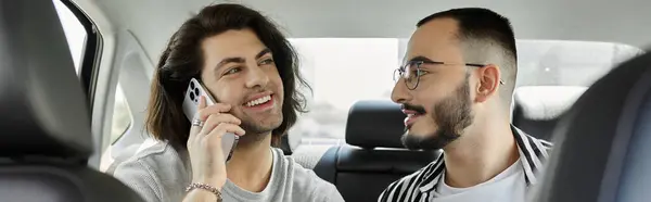 Two men in a car, one on a phone call, look at each other lovingly. — Stock Photo