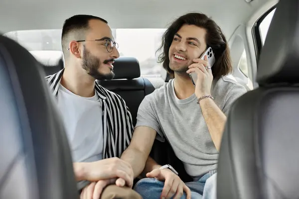 A gay couple in the backseat of a car, one on the phone, the other looking on with affection. — Stock Photo