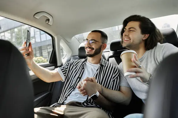 Two men smile in car backseat; one takes selfie, other holds coffee — Stock Photo
