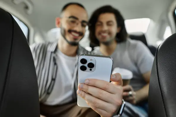 Two men in the backseat of a car, smiling and looking at a phone. — Stock Photo