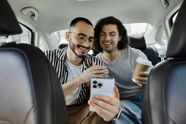 A loving gay couple shares a laugh while looking at a smartphone in the backseat of a car. — Stock Photo