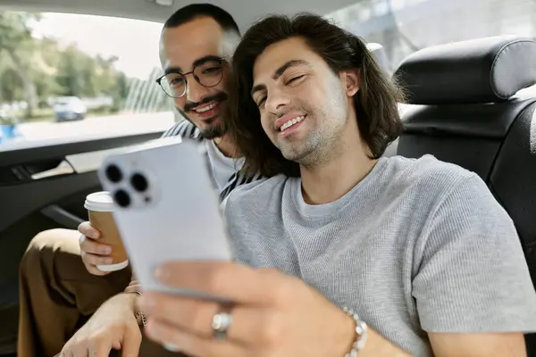 Due uomini ridono e guardano un telefono mentre guidano sul sedile posteriore di una macchina. — Foto stock