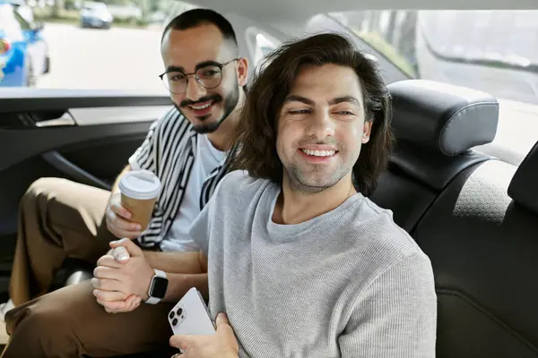 Two men smile and hold hands in the backseat of a car. — Stock Photo