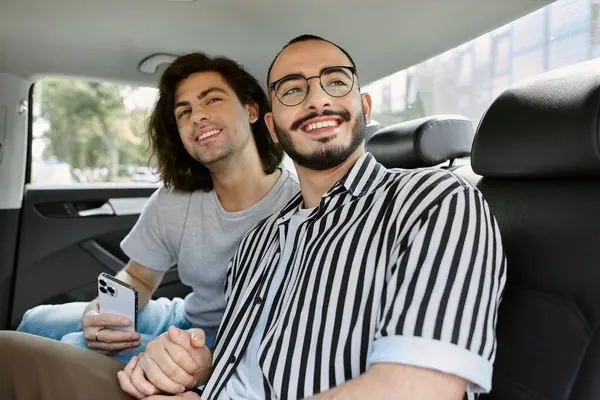 A happy gay couple enjoys a ride together, the man in the backseat holding a smartphone. — Stock Photo