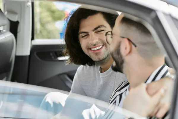 A gay couple sits in a car, laughing and smiling at each other. — Stock Photo