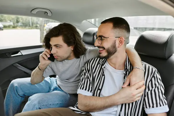 Two men enjoy a car ride together, one on the phone and the other looking lovingly at his partner. — Stock Photo