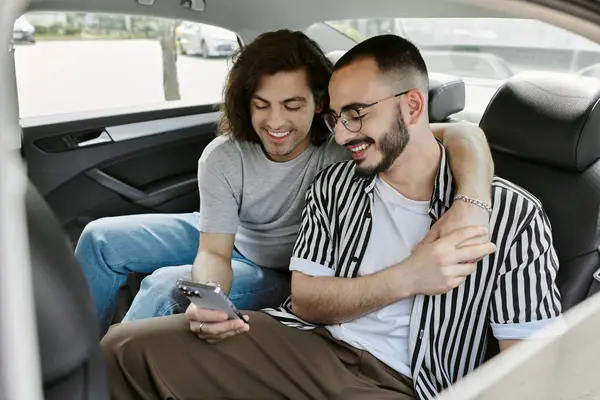 Um casal gay se senta no banco de trás de um carro, rindo e olhando para um telefone. — Fotografia de Stock