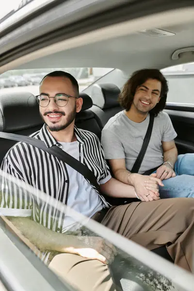Two men hold hands in the backseat of a car, smiling and looking happy together. — Stock Photo