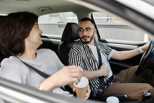 A gay couple shares a laugh and coffee while driving in their car. — Stock Photo