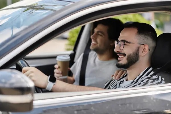 Two men laugh together while driving in a car. The passenger holds a cup of coffee. — Stock Photo