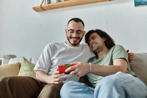 Two men share a laugh and a gift while sitting together on a couch. — Stock Photo