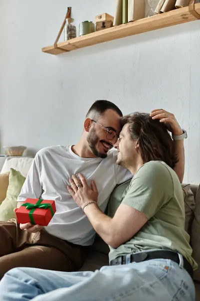 Two men are sitting on a couch, smiling at each other and holding a gift. — Stock Photo