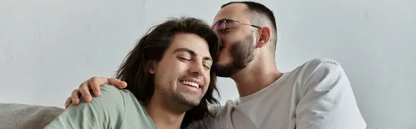 Una coppia gay si siede su un divano, un uomo bacia amorevolmente l'altro sulla fronte. — Foto stock
