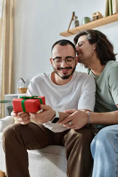 One man opens gift on couch, partner smiles and whispers — Stock Photo