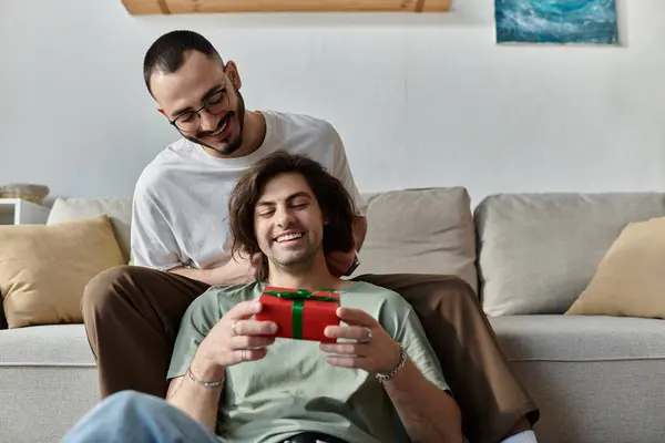 Gay couple cuddles on couch, man opens gift excitedly — Stock Photo