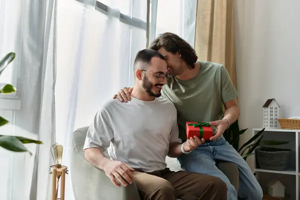 A couple sits by a window, one presenting a wrapped gift to the other. — Stock Photo
