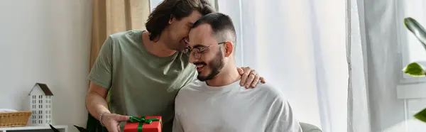 Two men in a loving relationship, one presenting a gift to the other, smiling and laughing together. — Stock Photo