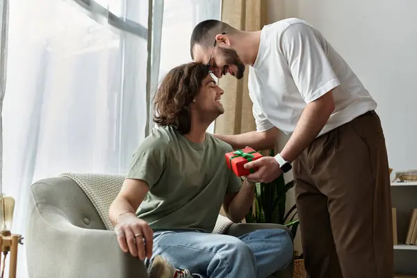 A gay couple shares a heartfelt moment, exchanging a gift in a bright living room. — Stock Photo