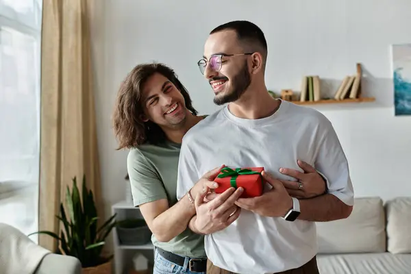 A gay couple embraces, one holding a gift for the other. — Stock Photo