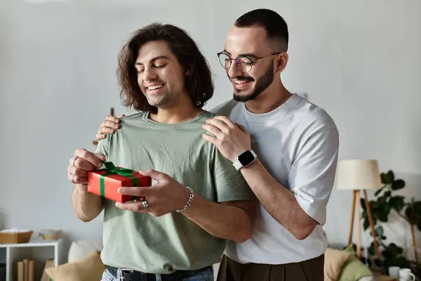 A man opens a gift from his boyfriend while standing in their home. — Stock Photo