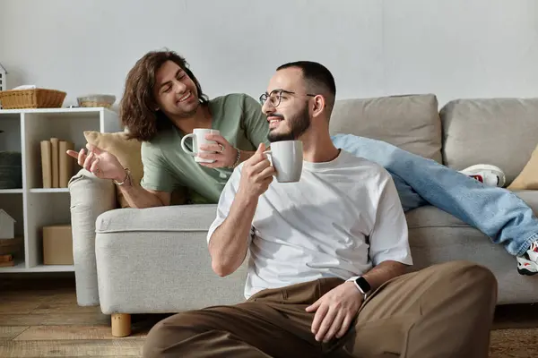 A gay couple enjoys a relaxed morning, sharing coffee and smiles on a comfortable couch. — Stock Photo
