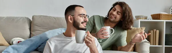 Dos hombres se relajan en un sofá, disfrutando de su café de la mañana. — Stock Photo