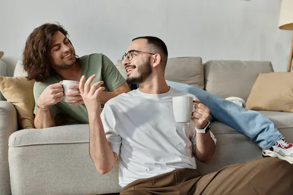 Two men relax on a couch, smiling and enjoying their coffee together. — Stock Photo