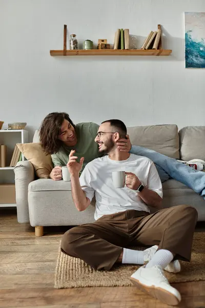 A gay couple enjoys a cup of coffee and a conversation on the living room floor. — Stock Photo