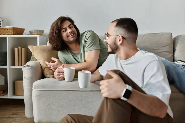 Two men share a warm smile and coffee while sitting on a couch. — Stock Photo