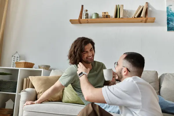 A gay couple relaxes on a couch, sharing a laugh and a drink. — Stock Photo