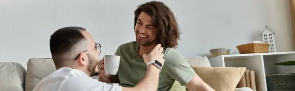 Two men share a laugh on a sofa, one with coffee — Stock Photo