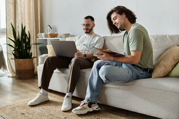 Two men relax on a couch together, one working on a laptop and the other reading a magazine. — Stock Photo