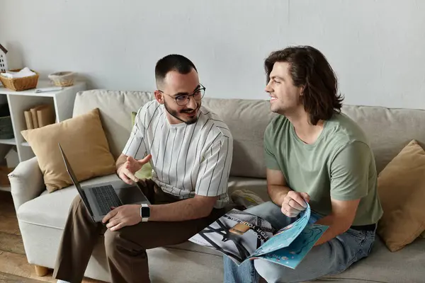 Due uomini su un divano, uno su un computer portatile, un'altra rivista di lettura, che ridono e si divertono a vicenda — Foto stock
