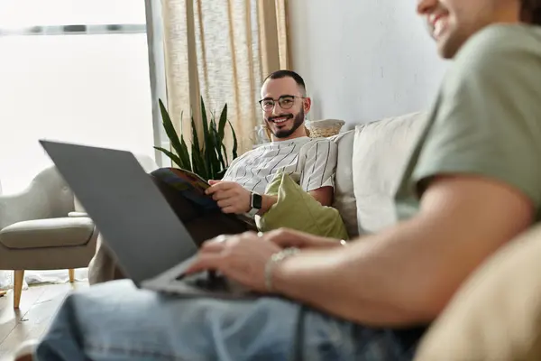 Couple relaxes on couch, one works on laptop while other reads magazine, sharing glance — Stock Photo