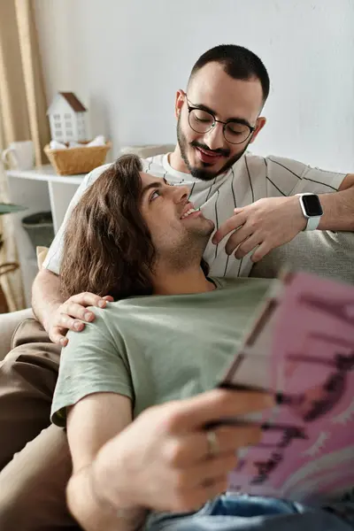Gay couple tenderly share a couch, one reads lovingly — Stock Photo